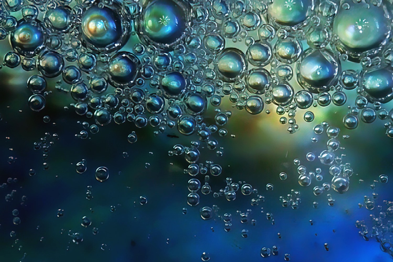A macro photograph of glowing green and blue bubbles suspended against a dark background, transitioning into deep blue at the bottom