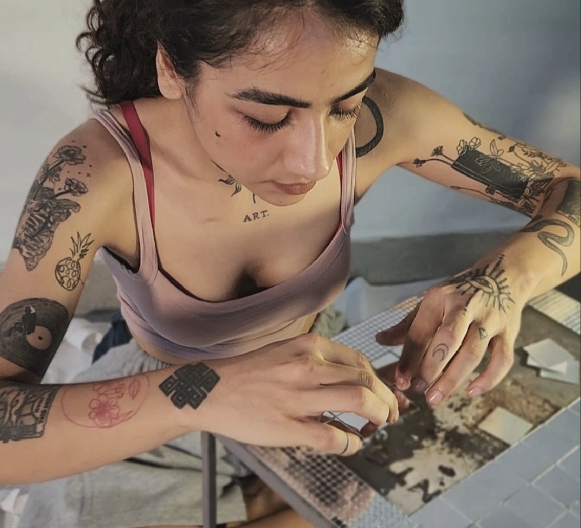 Close-up of Srishti Madaan, covered in tattoos, closely at work on a small piece at her worktable