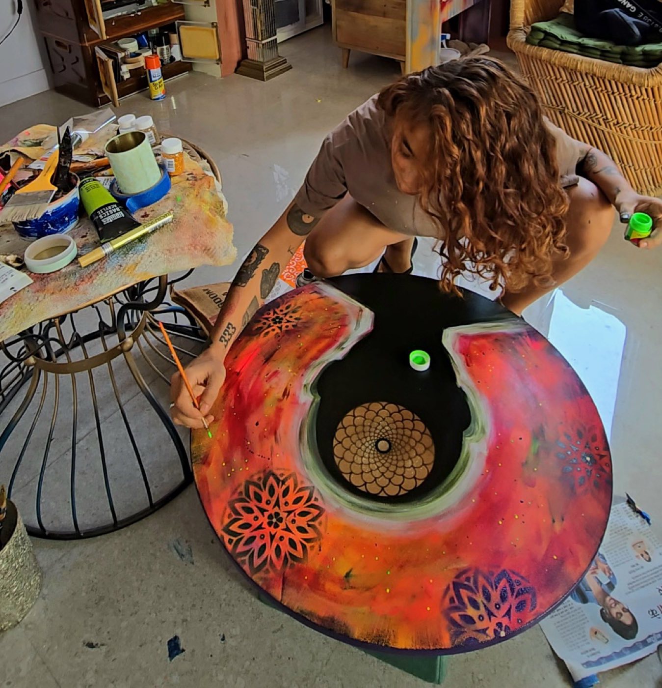Srishti Madaan crouched over a round wooden tabletop, hand-painting a red and orange mandala design with floral motifs